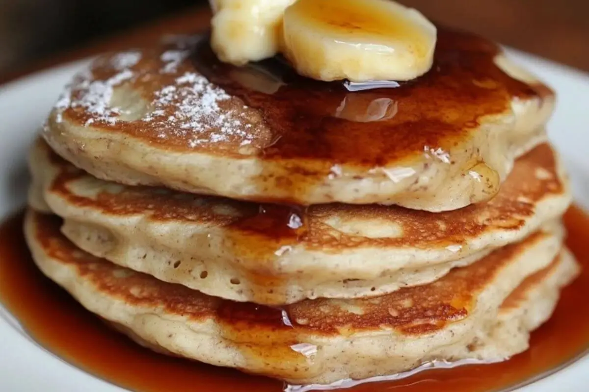 A stack of golden sourdough discard pancakes topped with butter and syrup on a plate.